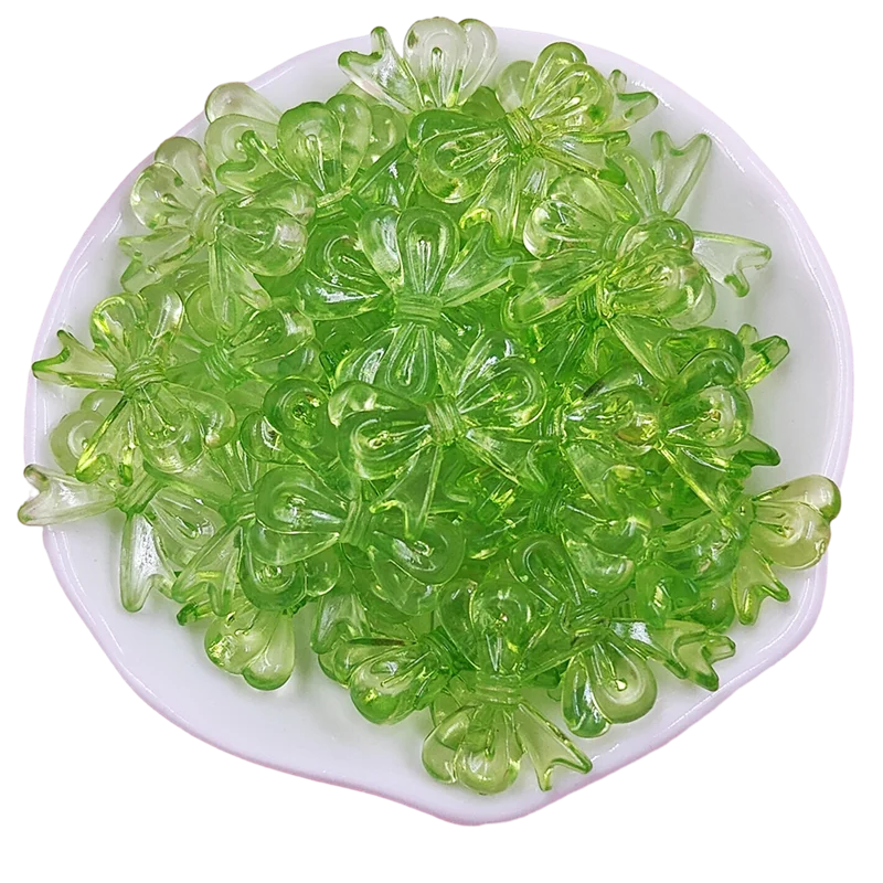 A pile of bright green acrylic bow beads for jewelry making arranged on a white dish.