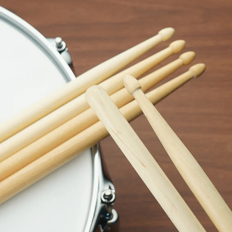 A set of light wood maple drumsticks resting on a white drum surface.