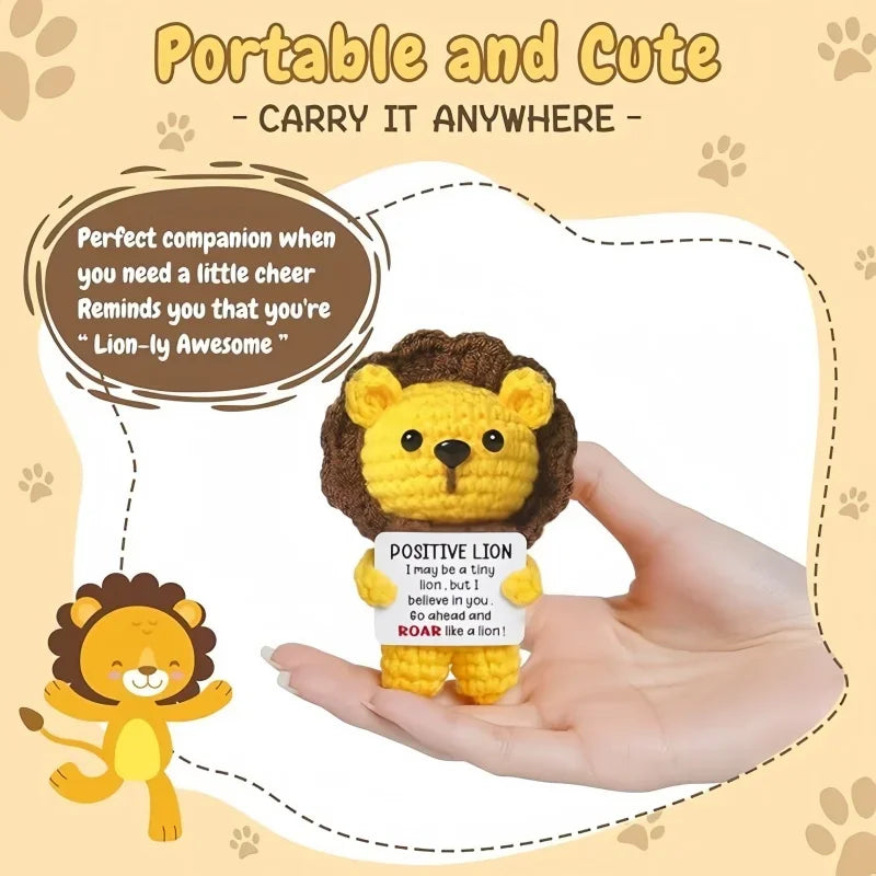 A hand holds a small crocheted yellow lion doll with a positive message card.