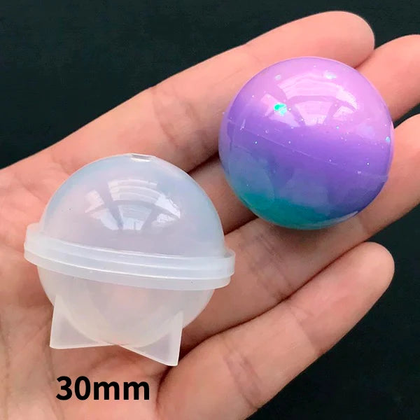 A hand holds a purple glitter sphere and a clear silicone mold for resin crafting.