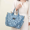 A woman holds a light blue floral canvas tote bag with multiple pockets against a white background.