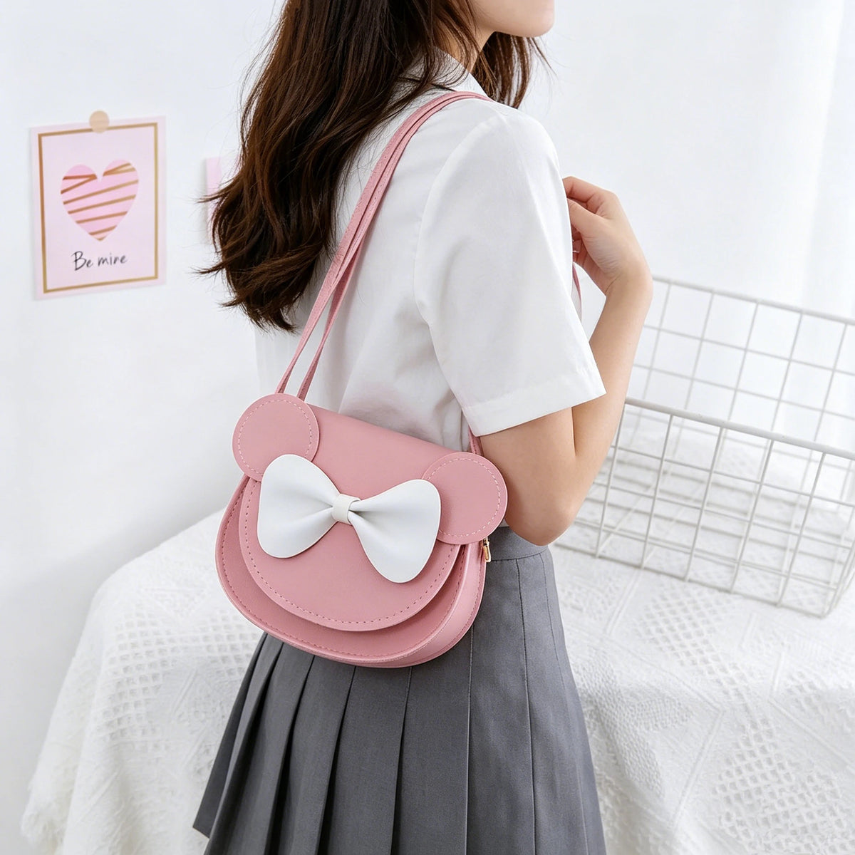 A pink kids' hard shell crossbody bag with mouse ears and a white bow worn by a girl.