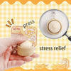 A hand is pressing a light-colored dumpling stress relief item onto a white plate.