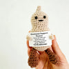 A hand holds a handmade crochet animal plush doll with a sign that reads Emotional Support Peanut