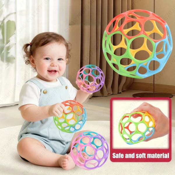 A baby is holding and playing with a colorful, porous sensory grip ball made of soft material.