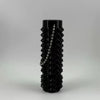 A black, cylindrical fidget toy with a textured spike pattern and a chain detail.