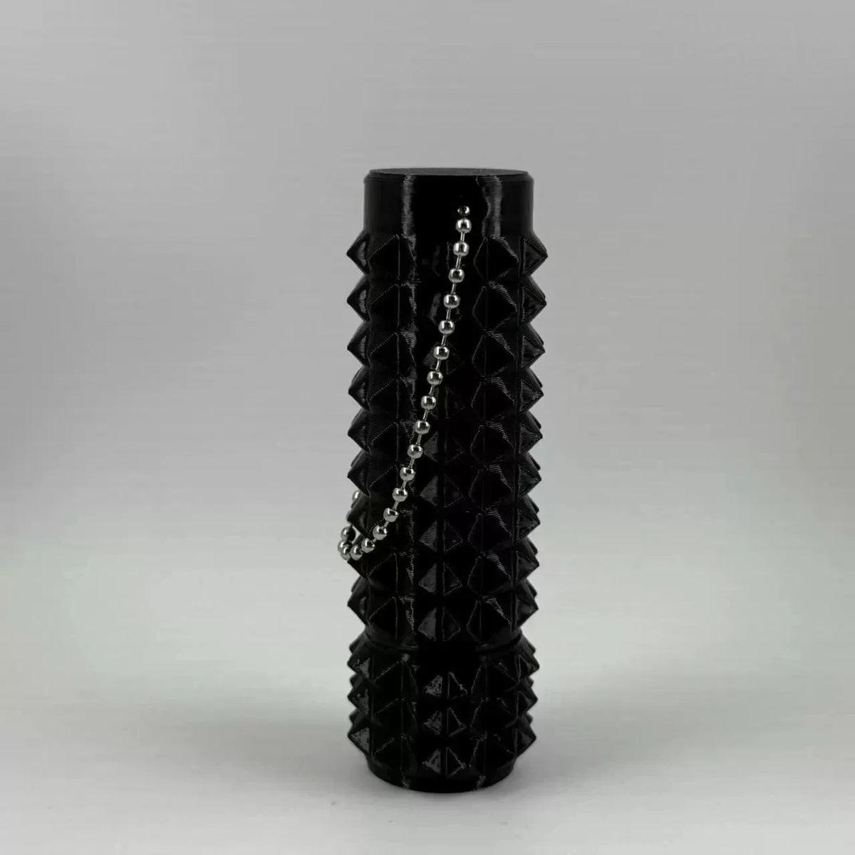 A black, cylindrical fidget toy with a textured spike pattern and a chain detail.