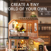 A wooden miniature dollhouse kit with LED lighting is being held, featuring a detailed shop facade and balcony.