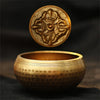 A close-up of a handcrafted brass Tibetan singing bowl resting on a dark surface.