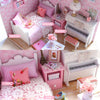 A pink and white miniature dollhouse setup featuring a princess crib, bed, piano, and furniture pieces.