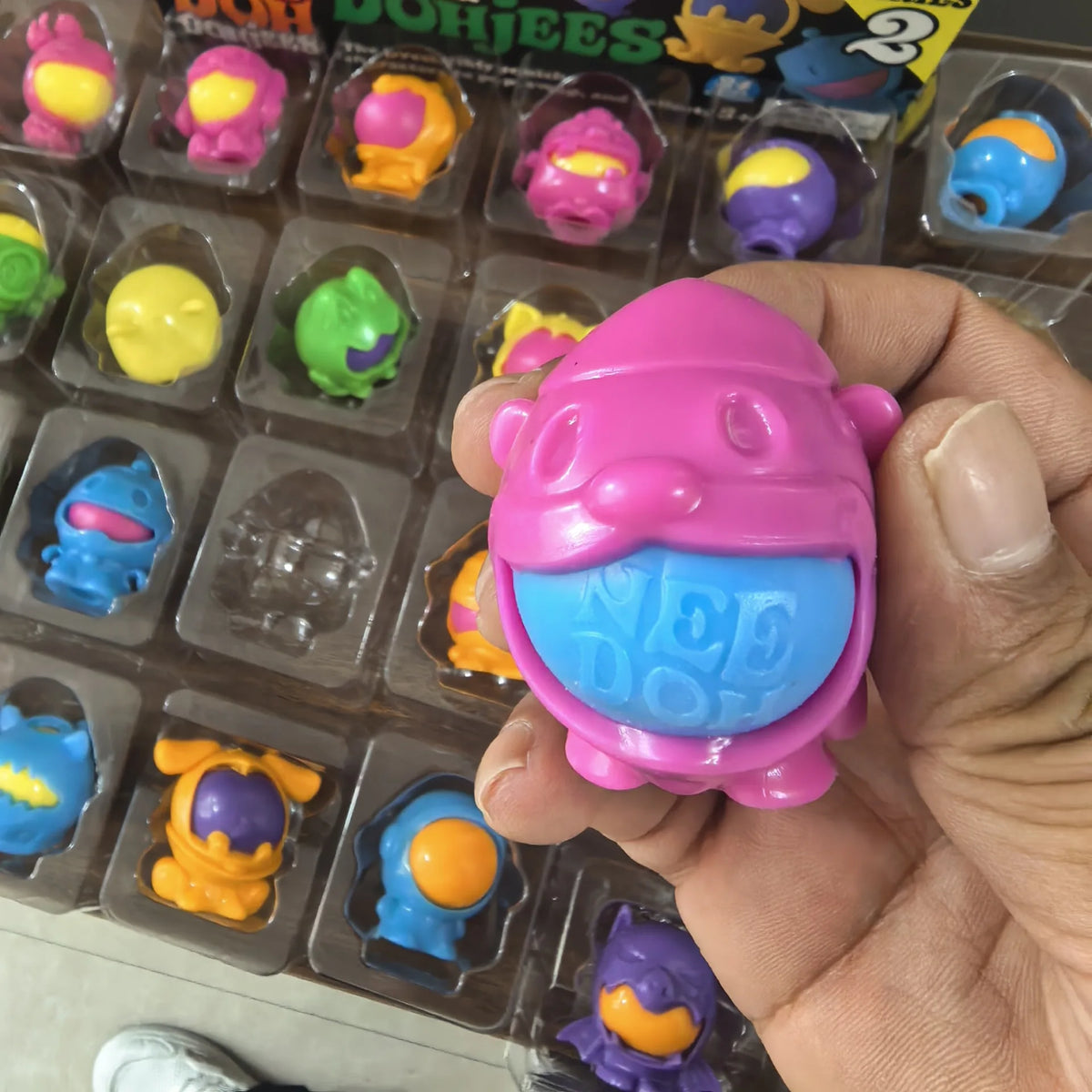 A hand holds a pink squishy fidget toy shaped like an emotional monster with blue accents.