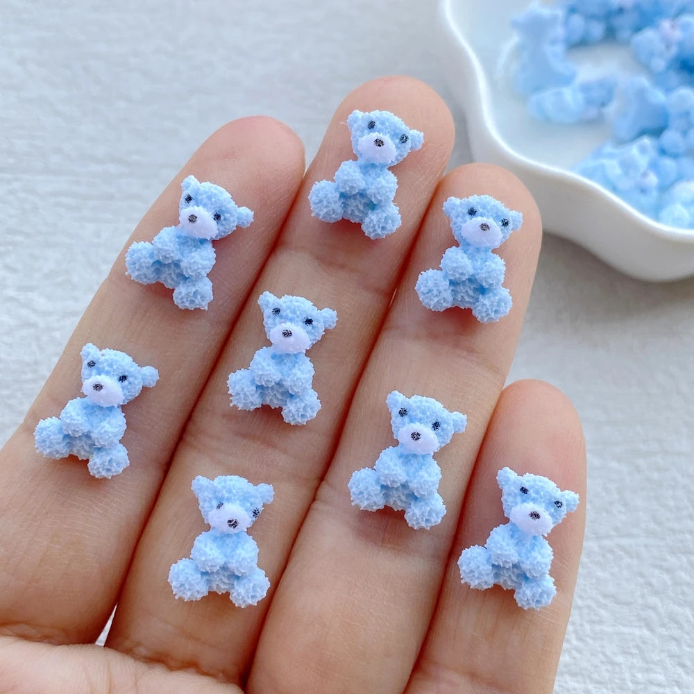 Ten fingers display small, light blue resin teddy bear charms for DIY crafts.