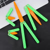 A set of orange and green 3D printed butterfly knife fidget toys lying on a black surface next to a laptop.
