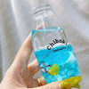 A hand holds a clear glass bottle filled with blue liquid labeled Chiboki drink cup toy