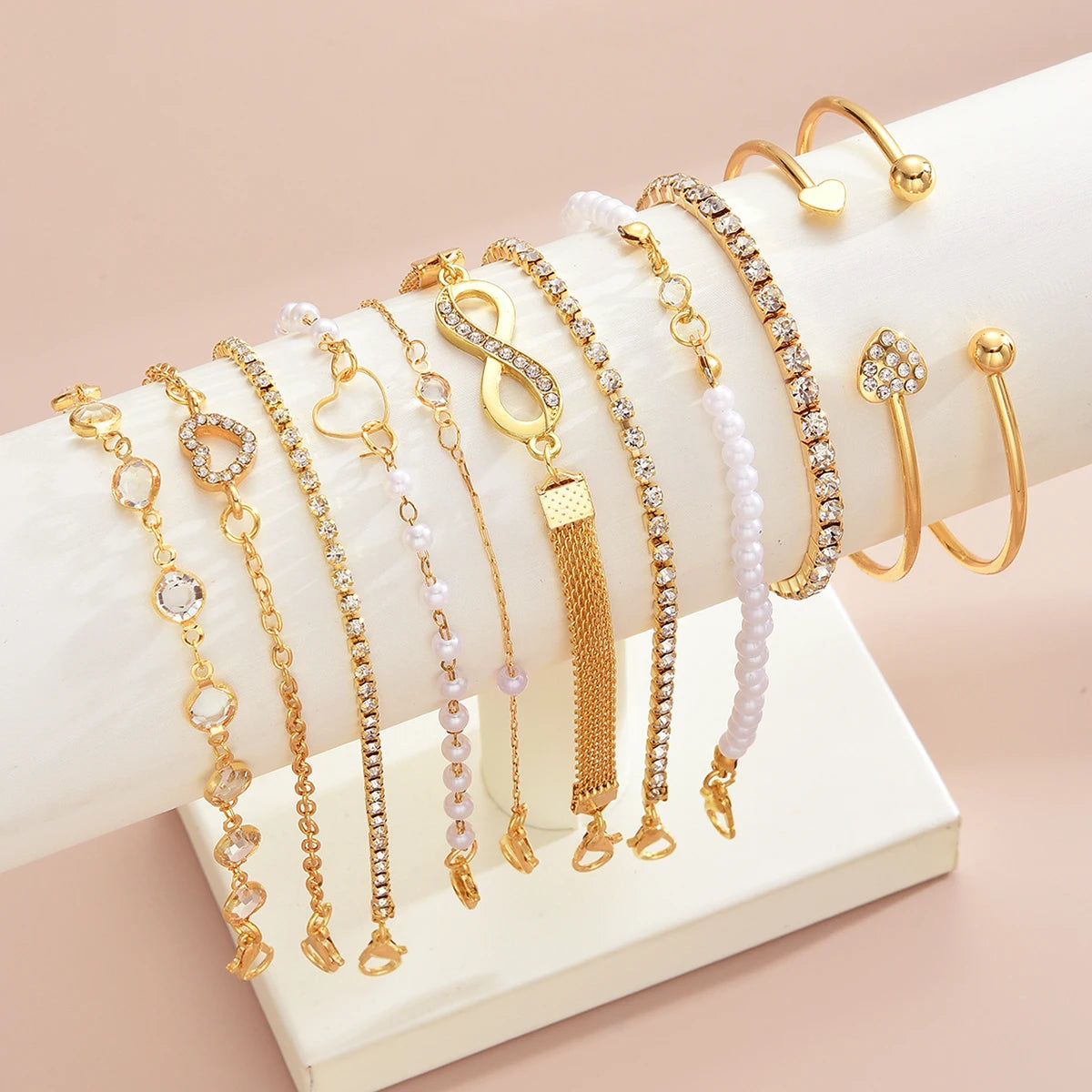 A collection of 11 gold and crystal bracelets featuring heart, infinity, and sign charms displayed on a white background.