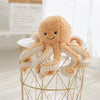 A fluffy, light brown octopus plush toy with white tentacles hanging from a gold wire stand.