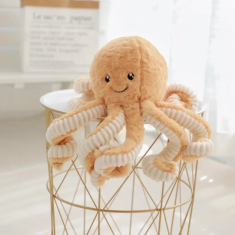 A fluffy, light brown octopus plush toy with white tentacles hanging from a gold wire stand.