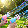 Hands hold a clear bubble gun with soft fan blades blowing bubbles in a sunny outdoor garden setting.