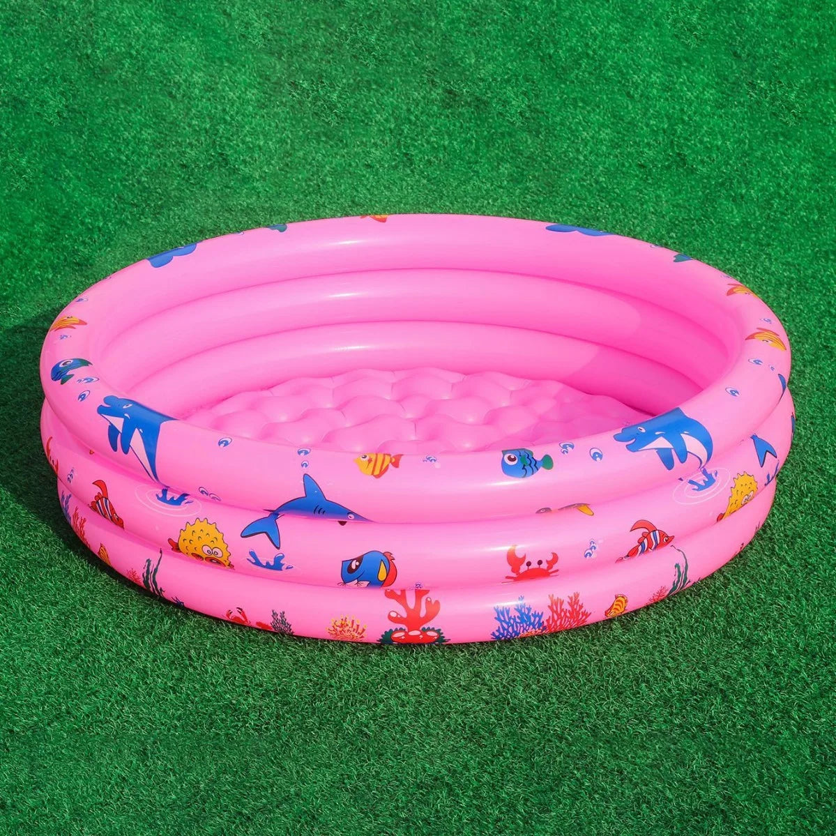 A pink inflatable kids play pool with a cartoon fish and sea creature design resting on green turf.