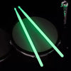 A pair of bright green glow-in-the-dark nylon drumsticks are displayed against a dark background.