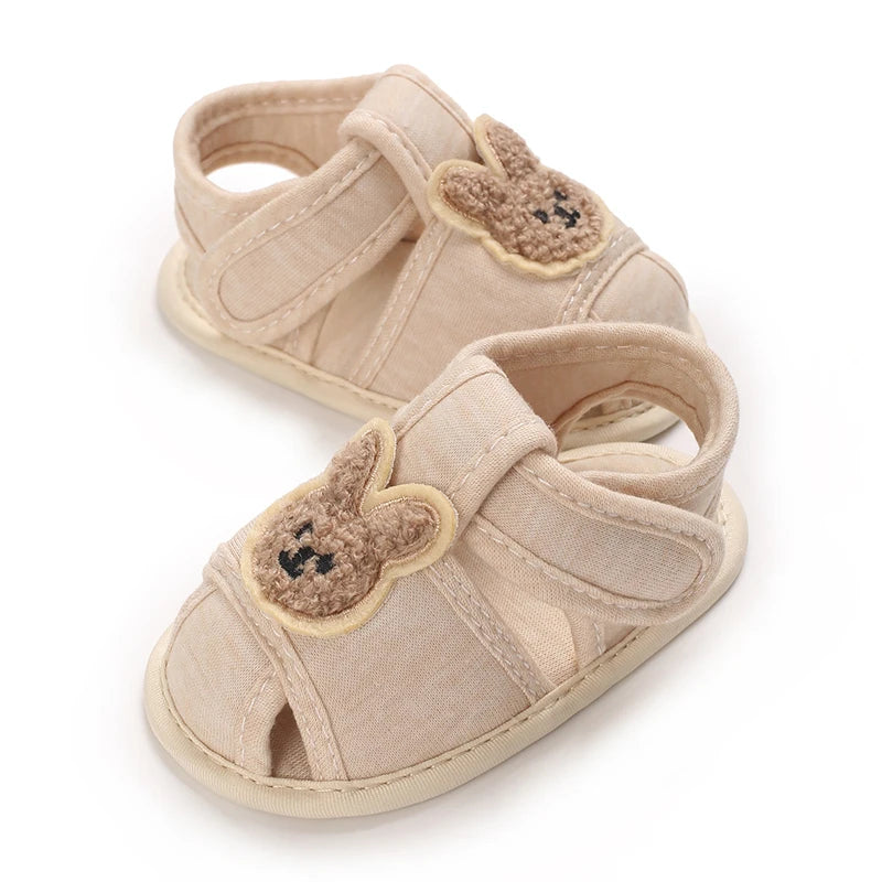 Pair of light beige soft sole sandals for baby's first steps featuring cute bear appliqués