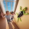 Two children are posing in a room with a wall-climbing RC gecko toy mounted on the wall.