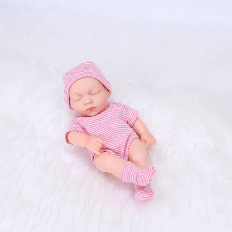 A realistic soft vinyl baby doll wearing a pink striped outfit and matching hat, lying on a white surface.