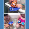 A hand holds a blue rubber fish bath toy with yellow fins and a small water squirting feature.