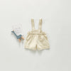 A pair of beige toddler denim rompers with straps and pockets displayed on a light gray background.