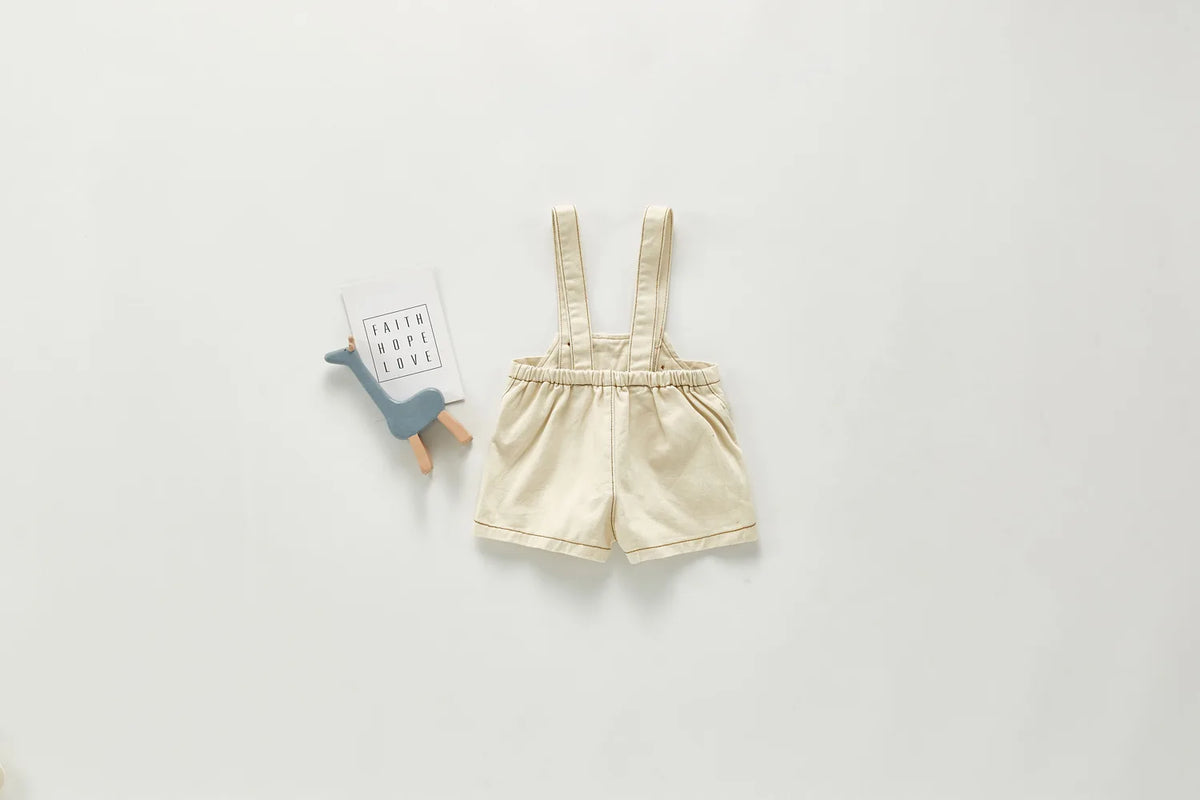 A pair of beige toddler denim rompers with straps and pockets displayed on a light gray background.