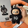 A hand holds a black plush toy resembling a rabbit with large eyes and a white toothy grin, set against an orange background.