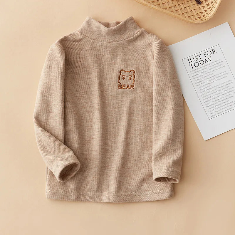 A beige long sleeve shirt for kids featuring a small brown bear embroidery on the chest.