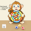 A cartoon monkey holding a dart board with a hook and three sticky balls on a wooden surface.