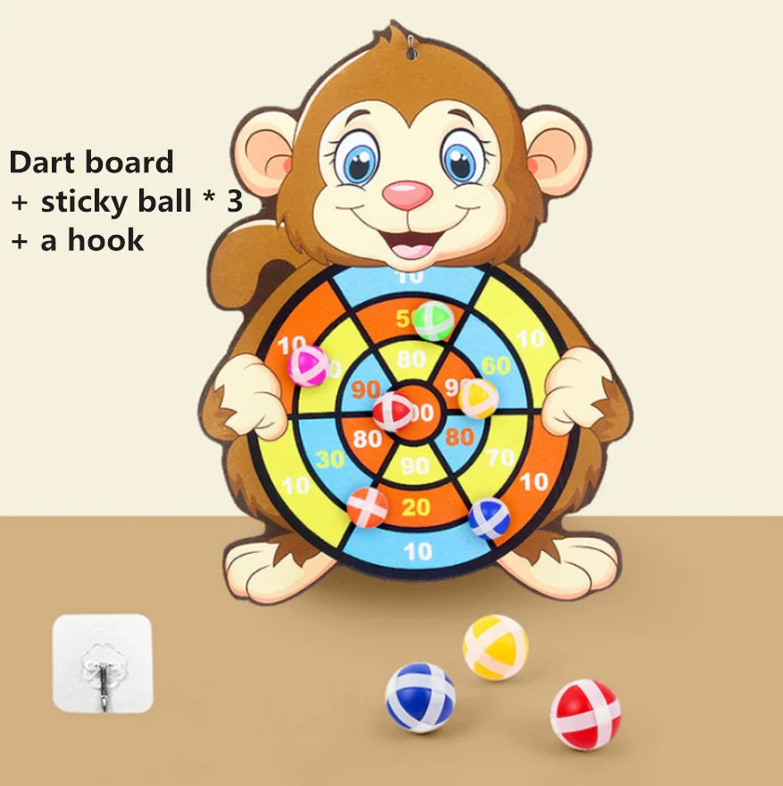 A cartoon monkey holding a dart board with a hook and three sticky balls on a wooden surface.