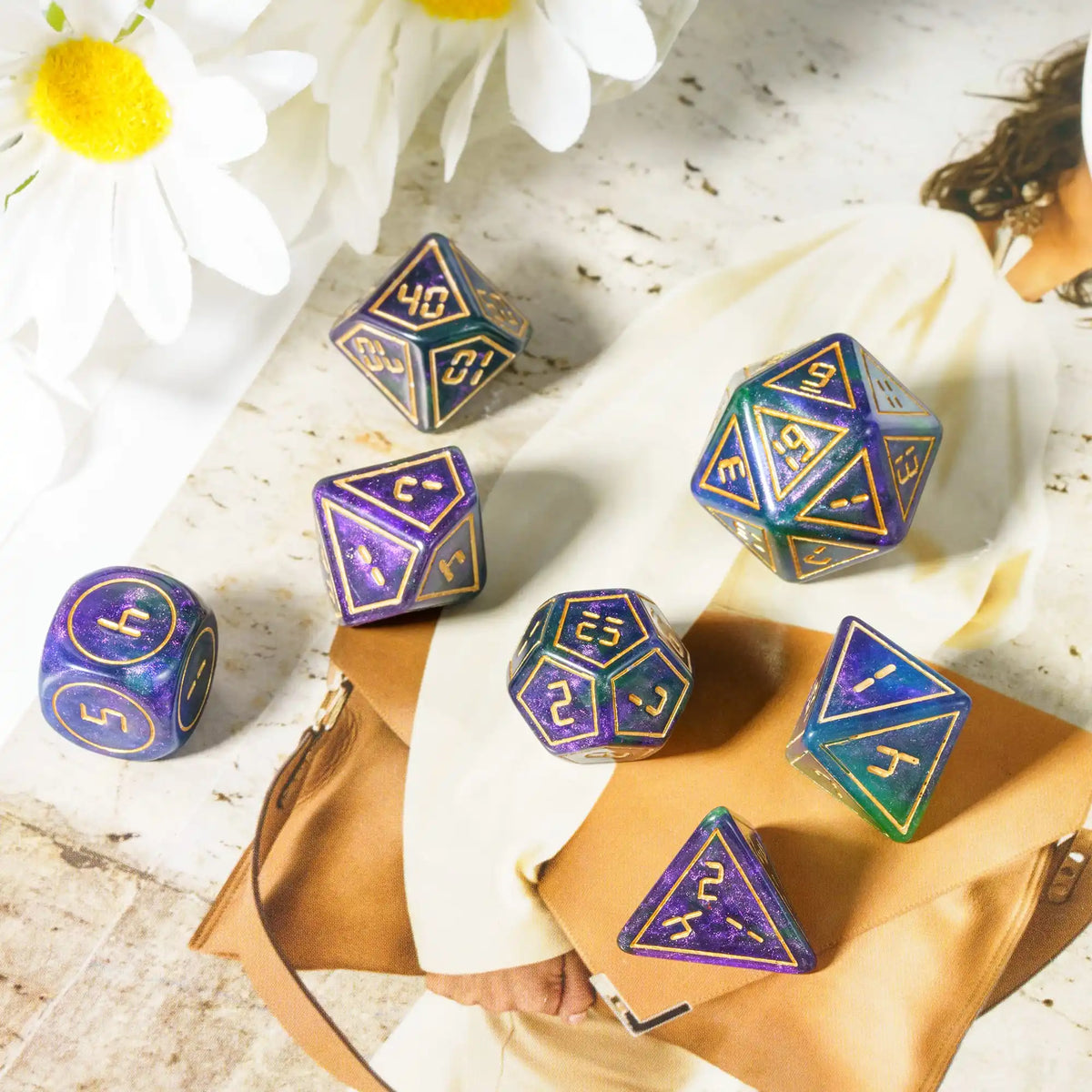 A set of seven resin polyhedral dice, including a d40 and d6, displayed on a light surface next to a leather-bound notebook.