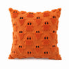 An orange, textured pillow cover featuring a pattern of small, black ghost faces.