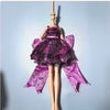 A fashion doll wearing a purple and black lace dress with sheer purple fabric wings.