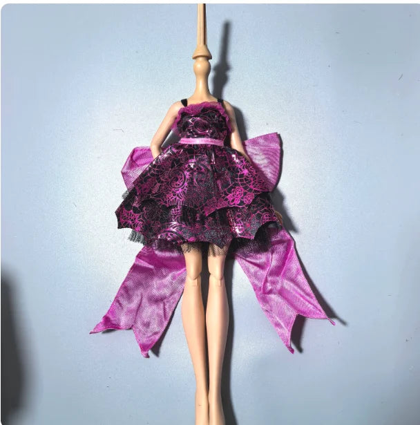 A fashion doll wearing a purple and black lace dress with sheer purple fabric wings.