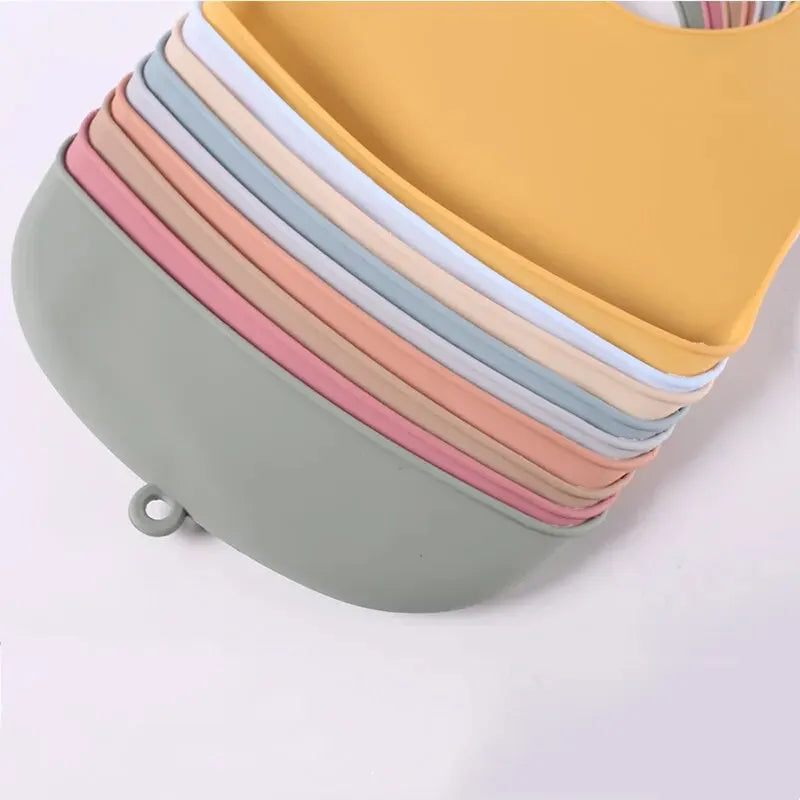 A stack of colorful silicone baby bibs with catch pockets displayed on a light gray dish.
