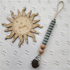 A wooden sun-shaped pacifier clip with a silicone teether attached to a gray beaded chain.