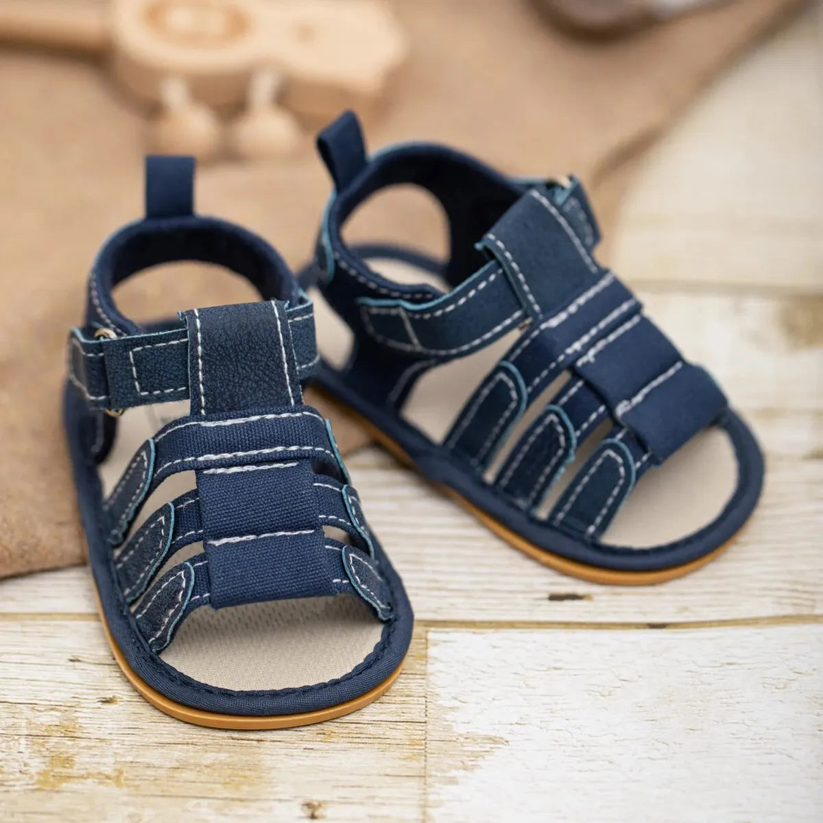 A pair of navy blue soft non-slip baby sandals for first walkers resting on a light wooden surface.