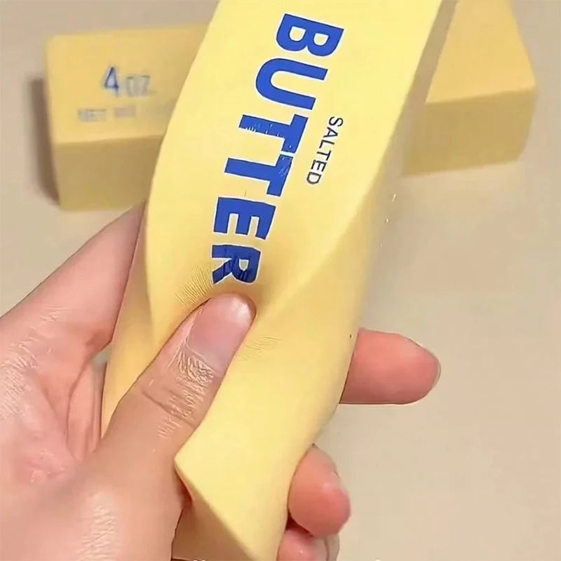 A hand holds a yellow salted butter stick fidget toy with the word BUTTER visible on it.