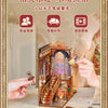 A wooden puzzle kit depicting a scene, with hands assembling the miniature diorama.