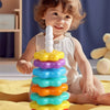 A toddler is playing with a colorful rainbow spin tower stacking toy made of plastic rings.