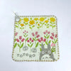 A soft stuffed animal featuring a cute gray cat design on a light green fabric with yellow and pink floral patterns.