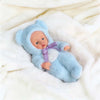 A realistic soft vinyl reborn baby doll wearing a light blue hooded outfit lying on white fur fabric.