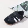 A pair of black baby first walkers shoes with white stripes and a soft sole resting on a white background.
