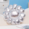 A silver plush cushion shaped like a large sunflower resting on a white surface.