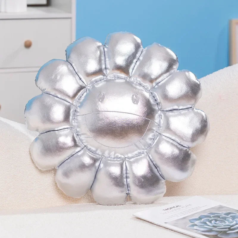 A silver plush cushion shaped like a large sunflower resting on a white surface.
