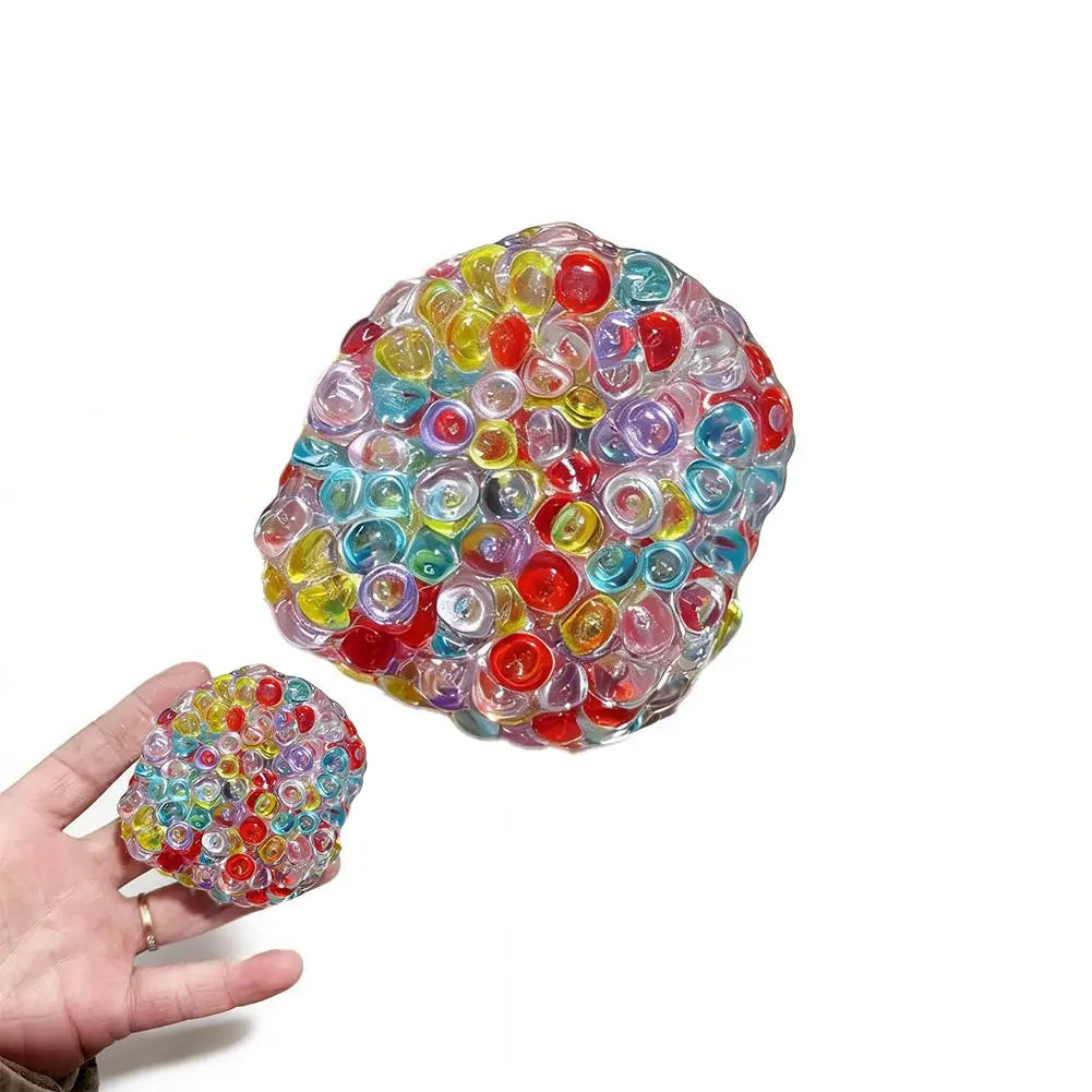 A hand holds a colorful, translucent squishy bead stress ball filled with various colored plastic beads.